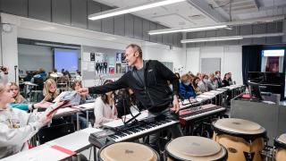 Musiikin opettaja ojentaa nuotteja opiskelijalle.